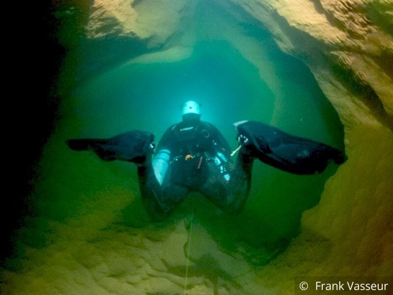 Plongeur équipé de palmes et lampe explorant une grotte sous-marine aux parois rocheuses jaunes.